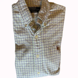 Rutig skjorta Polo Ralph Lauren  - Klassisk rutig skjorta från Polo Ralph Lauren i slim fit. Skjortan är vit med blå och gröna rutor, har knappar framtill och button-down krage. Broderad logga på bröstet. Tillverkad i mjuk bomull och långärmad modell.  Storlek M❤️‍🔥❤️‍🔥