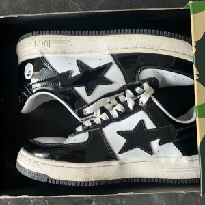 BAPE STA svartvita sneakers - Säljer ett par ikoniska BAPE STA sneakers i svart och vitt med glansig finish och den klassiska stjärnloggan på sidorna. Skorna har vit sula, svarta detaljer och vita skosnören. Kommer i originalkartong med camomönster. Perfekt för dig som vill sticka ut.                                                                         Pris kan 100% diskuteras vid snabb affär!