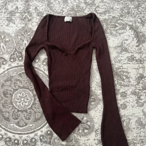 Mörkbrun ribbad långärmad topp - Säljer en mörkbrun ribbad topp med lång ärm och snygg v-ringad detalj vid bysten. Toppen har en slim passform och är tillverkad i ett stretchigt stickat material som sitter riktigt snyggt. Perfekt för en höstoutfit med kjol