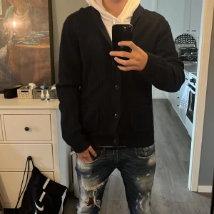 Stickad kofta från Dressman - Säljer en mörkblå kofta från Dressman med snygg sjalkrage och ribbad struktur. Koftan har två framfickor och knäpps med knappar framtill. Perfekt för lager-på-lager och passar till jeans 