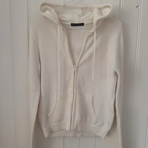 Vit stickad hoodie från Brandy Melville - Mysig vit stickad hoodie från Brandy Melville med dragkedja framtill, huva med snörning och två fickor. Perfekt för lager-på-lager och chill dagar. Långärmad och ribbade muddar för extra komfort.