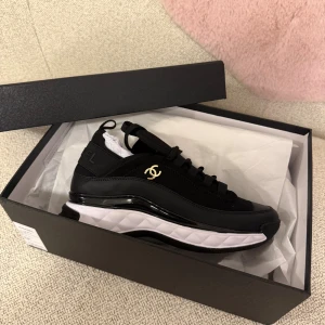 Svarta sneakers från Chanel - Säljer ett par svarta sneakers från C med vit och svart chunky sula och guldfärgad logga på sidan. Skorna har snörning, rund tå och är tillverkade i en mix av skinn och syntetmaterial. Snygg och sportig design med exklusiv känsla och tydlig C branding på hälen. Storlek 40 men känns mer som 39. Box och allt tillkommer