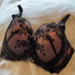 Svart-rosa blommig spets-BH från Hunkemöllers Noir-serieNoir - Säljer en svart-rosa BH från Hunkemöller med transparent mesh och blommigt spetsmönster. Axelbanden är justerbara och kanten har fina spetsdetaljer. Perfekt för dig som gillar en elegant och edgy stil. Storlek 80D. Sparsamt använd och givetvis tvättad.