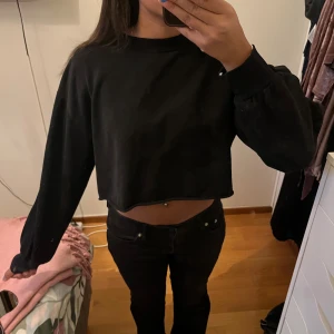 Svart croppad tröja från H&M Divided - Svart croppad tröja från H&M Divided med rund hals och långa ärmar. Enkel och stilren modell i mjuk bomul. Tröjan har en loose passform och ribbade muddar vid ärmslut.