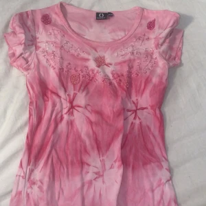 Rosa y2k topp med pärldetaljer - Säljer en rosa och vit y2k från Connect med korta ärmar. Toppen har coola pärldetaljer och broderier framtill vid halsringningen. Mjuk och skön bomullskänsla, perfekt för dig som gillar färg och unika mönster.