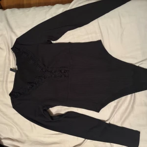 Svart ribbad topp med spets från H&M Divided - Svart långärmad topp från H&M Divided i ribbat material. Toppen har en snygg v-ringning framtill med dekorativ spetsdetalj som ger en extra touch. Perfekt att styla med jeans eller kjol för en trendig look. Endast använt den 2-3 gånger så den är i fint skick. Jag är 179 cm och den passar bra på mig. Fler foton kan skickas om önskas och pris kan diskuteras. 