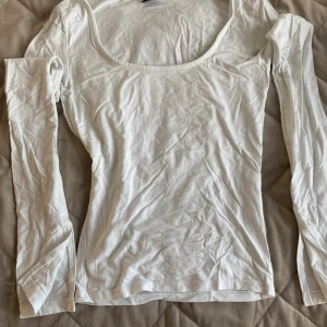 Vit långärmad topp från Gina Tricot - En basic vit långärmad topp från Gina Tricot i storlek XS. Toppen har en rundad, lite djupare urringning och är tillverkad i ett mjukt och stretchigt material som sitter skönt på kroppen. Perfekt att styla med jeans eller kjol.