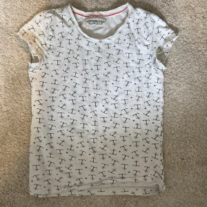 Vit t-shirt med ankare från Hampton Republic - Vit t-shirt från Hampton Republic med marinblå ankare och små stjärnor över hela tyget. Klassisk rund halsringning och korta ärmar. Tillverkad i mjuk bomull, perfekt för en avslappnad och nautisk look. Jag säljer den nu då den inte är i min stil längre🥰