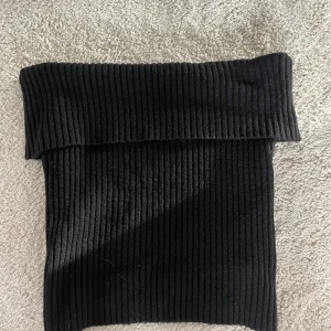 Svart ribbad tubtopp - Säljer en svart ribbad tubtopp med bred uppvikt kant upptill. Toppen är tight och har en stilren look som passar perfekt till höga jeans eller kjol. Materialet är stretchigt och bekvämt, vilket gör den enkel att bära hela dagen.