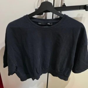 Svart croppad tröja från Lager 157 - Svart croppad tröja från Lager 157 i modellen Frida. Tröjan har rund halsringning, korta ärmar och är tillverkad i 100% bomull. Enkel och stilren design som passar perfekt till jeans eller kjol.