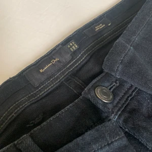 Massimo Dutti Svarta Byxor GRATIS FRAKT - Slim Fit snygga svarta jeansbyxor från Massimo Dutti i klassisk rak modell. Byxorna har fem fickor, diskreta sömmar och stilren knapp med logotyp. Materialet är mjukt och slitstarkt, perfekt för en clean och tidlös look.