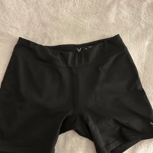 Svarta träningstights-shorts från SOC - Svarta, tighta träningstights-shorts från SOC. De har en enkel och clean design med midwaist passform och är gjorda i ett stretchigt syntetmaterial som andas. Perfekta för gymmet eller löprundan.