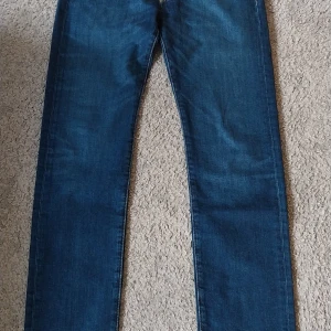 Levi's 501 blå jeans W29 L32 - Helt nya oanvända Levi's 501 jeans i blå denim med raka ben och normal passform. Snyggt mellanblå färg, femficksmodell och ikonisk läderpatch bak i midjan. Perfekta för dig som gillar tidlös stil och vill ha ett par jeans som funkar till allt.