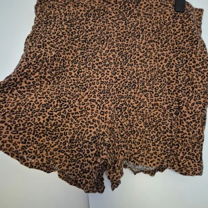 Leopardmönstrade shorts från Lindex - Snygga shorts från Lindex i leopardmönster med bruna och svarta toner. De har en lös passform och är tillverkade i ett lätt och luftigt material, perfekt för varma dagar. Resår i midjan för extra komfort och en trendig vibe.