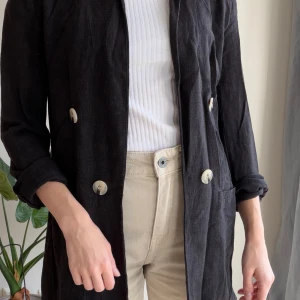 Svart kavaj med knappar - Snygg svart kavaj med dubbelknäppning och stora ljusa knappar. Jackan har en rak passform och är tillverkad i ett mjukt tyg som ger en chill och stilren vibe. 