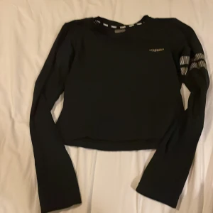 Svart croppad träningströja Stronger - Svart långärmad croppad träningströja från Stronger med coola prickiga detaljer i silver på ena ärmen. Tröjan har rund hals och logga på bröstet. Perfekt för gymmet eller sport. Snygg och bekväm passform. nyskick!!!