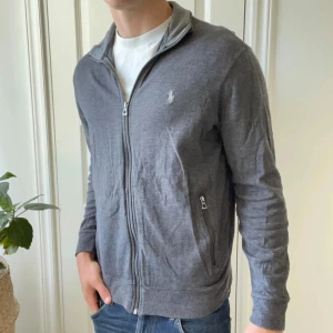 Ralph Lauren full zip / cardigan - Skön full zip, modellen bär M och är 180,75 kg. Inga defekter förutom ett minimalt håll som inte märks vid fickan. Finns två fickor med dragkedja.  
