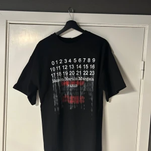 Svart Maison-Margiela t-shirt - Cool svart t-shirt från Maison Martin Margiela med tryck av siffror och text på bröstet. Klassisk passform och rund halsringning. Perfekt för dig som gillar streetwear och designerplagg. Köpt i Portugal hos dem själva. Skriv vid frågor MVH VIGGO