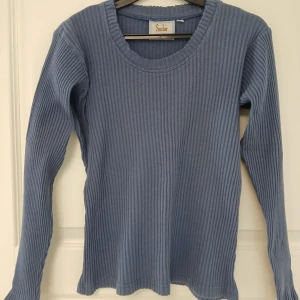 Långärmad tröja by Kappahl - Blå långärmad tröja. Tillverkad i bomull. Perfekt för dig som gillar en stilren design. Tröjan har naturligtvis tvättats. Se bilder för skick och passform. Storlek 38/40 enligt lappen. Armhåla till armhåla är cirka 49 cm. Axelsöm till ärmslut är cirka 55 cm. Tvättas i 60 grader.