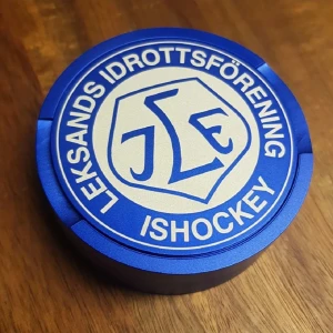 Leksands IF Ishockey snusdosa - Snygg ishockeypuck med Leksands IF:s logotyp i blått och vitt. Perfekt för samlare eller fans. Pucken ser ut att vara i nyskick utan synligt slitage eller repor. Passar både som dekoration och för spel.