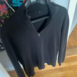 Svart långärmad tröja selected home  - Svart långärmad tröja  med stilren half zip-dragkedja vid halsen. Tröjan har en enkel design med ribbad krage och är tillverkad i mjuk bomull som känns skön mot huden. Perfekt för dig som gillar minimalistisk stil.