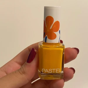 Pastel gul nagellack med blommor - Säljer ett coolt gult nagellack från Pastel i en fyrkantig glasflaska. Locket är vitt med orange och blå blommor som ger en färgglad vibe. Perfekt för dig som vill ha riktigt poppande naglar! Volymen är 13 ml och färgnumret är 353.