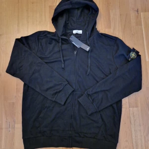 Svart hoodie från Stone Island - Säljer en helt ny Svart zip-hoodie från stone island. Står storlek 2XL men passar XL!!