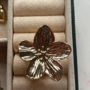 Guldfärgad blomring i metall - Stor statementring i guldfärgad metall formad som en blomma med fem blad. Ringen har en öppen baksida som gör den justerbar i storlek. Blommans yta är lätt vågig och reflekterar ljuset snyggt. Har aldrig använt 💕