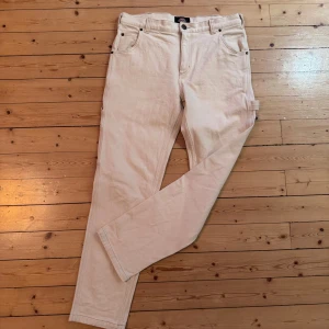 Beiga cargobyxor från Dickies W34/L34 - Säljer ett par beiga cargobyxor i jeanstyg från Dickies med raka ben och flera praktiska fickor. Byxorna har klassisk passform, hällor för bälte och är tillverkade i slitstarkt jeanstyg. Perfekta för dig som gillar streetwear och funktionella detaljer.