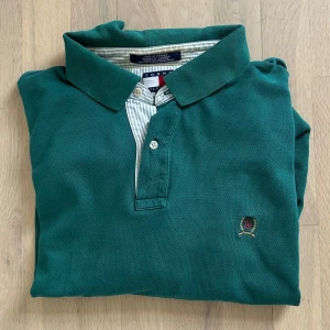 Grön pikétröja Tommy Hilfiger - Snygg grön pikétröja från Tommy Hilfiger med klassisk krage och korta ärmar. Tröjan har två knappar vid halsen och ett broderat emblem på bröstet. Tillverkad i mjuk bomull som känns skön mot huden. Perfekt för dig som gillar stilren och sportig look.