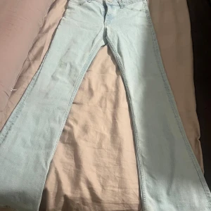 Ljusblå utsvängda jeans från H&M - Säljer ett par ljusblå jeans från H&M med flared leg och låg midja. Byxorna har justerbar midja och klassisk femficksdesign. Materialet är en mix av bomull, polyester och elastan för en skön stretchig känsla. Perfekta för dig som gillar retrovibbar och snygg passform.