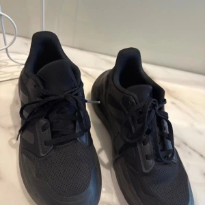 Svarta Adidas skor unisex  - Säljer ett par helsvarta Adidas sneakers med klassiska tre ränder på sidan. skorna har snörning. Perfekta för dig som gillar en clean och sportig look. Funkar för tjejer och killar. Bara använd några gånger 