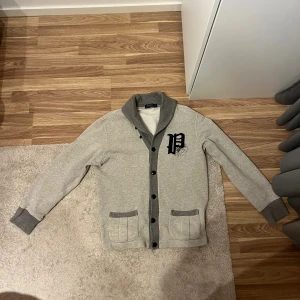Grå kofta från Polo Ralph Lauren - Snygg grå kofta från Polo Ralph Lauren med mörkare grå detaljer vid krage, knappslå och fickor. Kom pm för mera info eller bilder! 