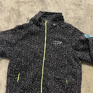 Svart vindjacka Top&Sky Kids - Svart vindjacka med vitt prickigt mönster från Top&Sky Kids. Jackan har gul dragkedja och detaljer samt en cool patch med kompass på ärmen. Perfekt för utomhusaktiviteter och äventyr.