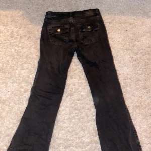 Svarta lågmidjade jeans - Ett par nästan oanvända svarta low waist jeans med knappar på bakfickorna. Väldigt sköna och sitter bra.
