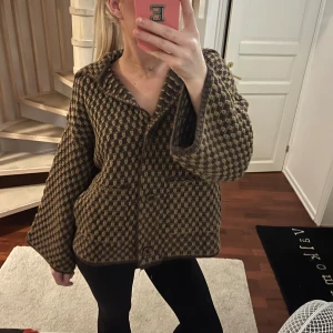 Brun mönstrad cardigan jacka från Zara - Säljer en oversized cardigan jacka från Zara i brun och beige med rutigt mönster. Jackan har stora knappar framtill, bred krage och långärmade ärmar. Stickad i mjukt material som ger en chill och trendig vibe. Perfekt för lager-på-lager och att hålla sig varm.