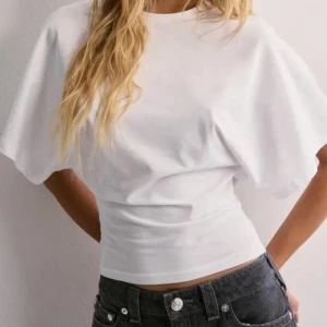 Vit croppad topp med knyt i ryggen - Säljer en vit croppad topp med korta ärmar och rund hals. Toppen har en cool öppen rygg med långa band som knyts baktill för en snygg siluett. Tillverkad i mjuk bomull, perfekt för dig som gillar trendiga och bekväma plagg med lite edge.