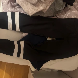 Svarta leggings med vita ränder - Svarta leggings från Stronger med två vita ränder på varje ben. Tillverkade i stretchigt syntetmaterial som passar perfekt för träning. Hög midja och tight passform för en sportig look. 