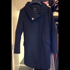 Svart kappa från Bershka - Stilren svart kappa från Bershka med bred krage och snygga ficklock. Kappan har både dragkedja och dekorativa knappar framtill. Perfekt för dig som gillar klassisk look med modern twist.