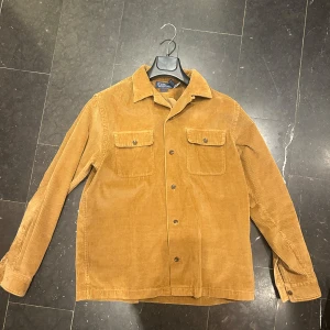 Overshirt - Snygg overshirt i klassisk brun manchester från Polo Ralph Lauren. Modellen är Classic Fit med två bröstfickor med knappar och långa ärmar. Perfekt för lager-på-lager och har en cool vintage-vibe. Stängs med knappar framtill och har en mjuk, strukturerad känsla. Köpt för 1800kr på NK.