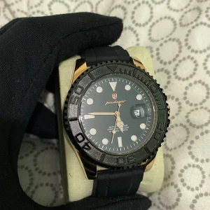 Svart gummi med rosé guld platerad poedagar klocka  - Svart gummi poedagar med guld rosé platerade detaljer rostfritt stål 