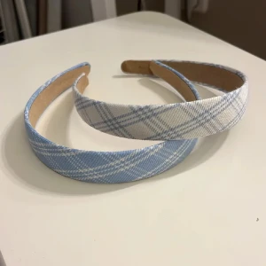 Två rutiga diadem i blått och vitt - Säljer två breda diadem med rutigt mönster i ljusblått och vitt. Perfekta för att ge en söt och preppy touch till din look. Bekväma att bära hela dagen och passar till både utsläppt och uppsatt hår.