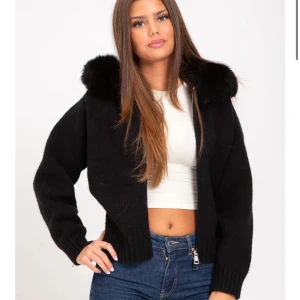 Svart kofta med äkta päls och dragkedja - Säljer en svart kofta med fluffig fuskpäls vid kragen och dragkedja framtill. Koftan har ribbade muddar och en loose passform som ger en chill vibe. Perfekt att slänga på sig när det är lite kyligt ute.