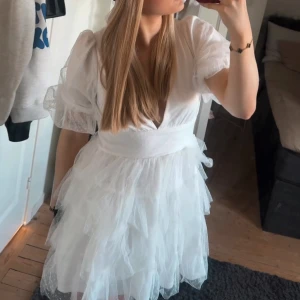 Vit student/ sommar klänning - Superfin vit oanvänd klänning med lappen kvar, perfekt till studenten. Den har volanger av tyll och är v-ringad. Klänningen har puffiga korta ärmar och en öppen rygg. Den har även en dragkedja där bak för att lättare få på klänningen. Den är i storlek M och passar mig som i vanliga fall brukar ha S/M