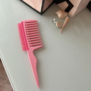En kam för att styla lockigt hår - En rosa kam som man kan använda för att styla blött, lockigt hår. Den har två sidor, en som har större mellanrum mellan borstpinnarna, och en som har väldigt små mellanrum och små och korta borstpinnar.