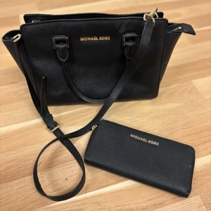 Svart handväska & plånbok Michael Kors - Snygg svart handväska i skinn från Michael Kors med matchande plånbok. Väskan har guldfärgade detaljer, dubbla handtag, axelrem och flera fack med dragkedja. Plånboken har gott om plats för kort och mynt, även den med guldfärgad dragkedja. Äkta!! 750kr för båda! 600kr för väska och 300 kr för plånbok!