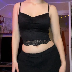 Croppad linnetopp med spets - Svart croppad linnetopp från FB sister med tunna axelband och snygg spetskant nedtill. Toppen har en lätt rynkad detalj vid bysten och är tillverkad i mjuk polyester med spetsöverdrag. Perfekt för dig som gillar en stilren och feminin look. Passar XXS-S tror jag.