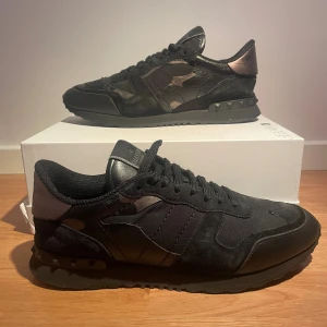 Valentino Rockrunner svarta sneakers - Svarta Valentino Rockrunner sneakers med coola kamouflagedetaljer och nitar på sulan. Skorna har en mix av mocka, skinn och textil, samt snörning framtill. Snygg och sportig siluett som sticker ut med sina mörka toner och exklusiva materialval. ❗️❗️❗️Pris kan diskuteras!❗️❗️❗️