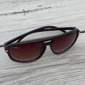 solglasögon från Vestimo - Snygga solglasögon från Vestimo med vinröda bågar och matchande tonade glas. Modellen har en klassisk pilotform med metalliga detaljer vid sidorna och näsbryggan. Perfekt accessoar för att lyfta din stil i sommar.