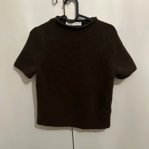 Brun stickad topp från Zara - Mysig brun stickad topp från Zara med korta ärmar och enkel, rak passform. Perfekt för lager-på-lager och funkar lika bra till jeans som kjol. Tjockare material som ger en cool och avslappnad vibe.